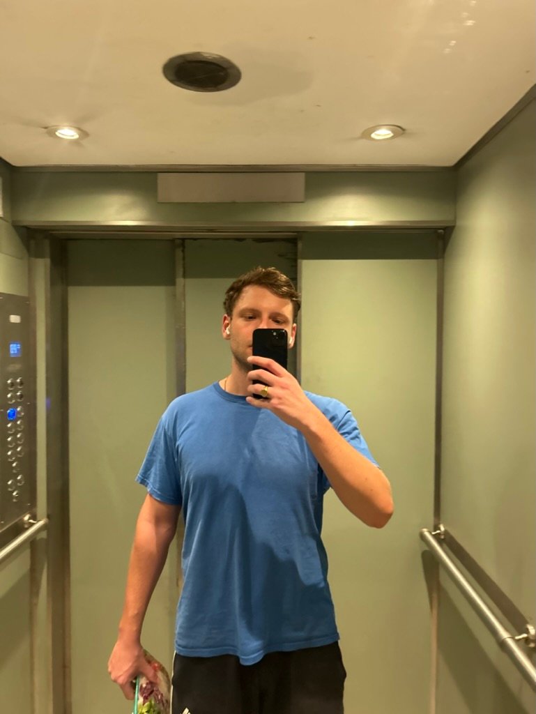 Man in running clothes taking a post-run mirror selfie in an elevator, holding fresh vegetables