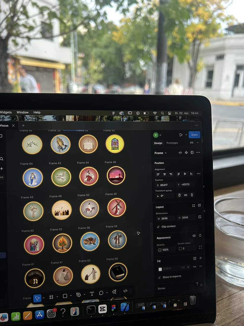 Bible-themed icons being designed in the Holy Focus app, shown on a laptop in a café.