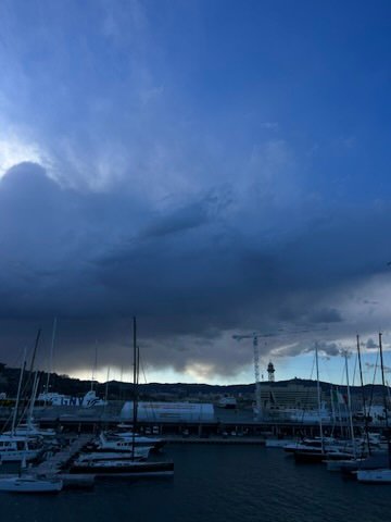 A marina filled with docked sailboats under a dramatic, dark blue sky with looming storm clouds.
