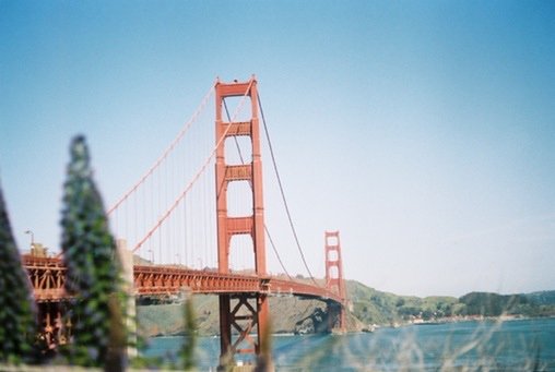 A softly focused photo of the Golden Gate Bridge stretching across the blue water on a clear day with hills in the background.