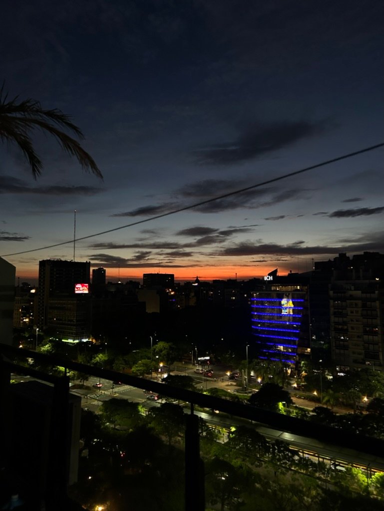 A city skyline at night with glowing building lights and a faint orange sunset on the horizon