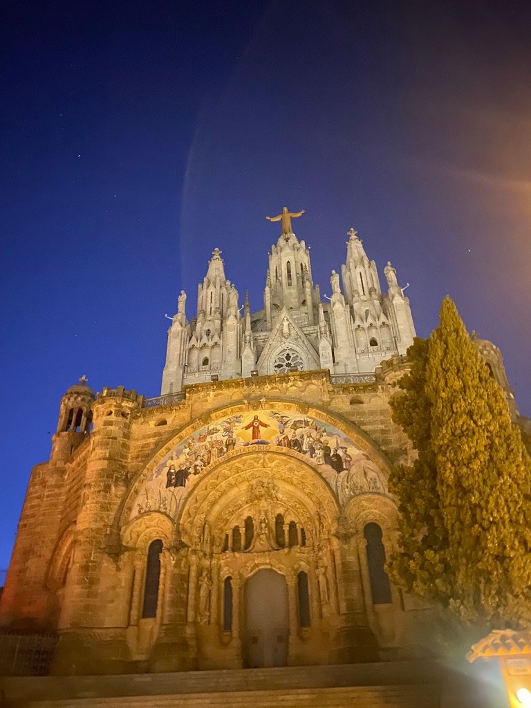 A majestic basilica illuminated at night with a statue of Christ standing atop its central tower, arms outstretched beneath a starry sky.