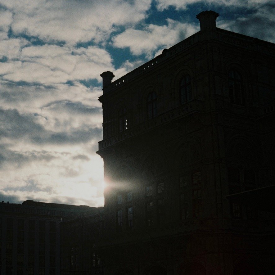 Sunlight breaks through behind the corner of a historic building under a cloudy sky.