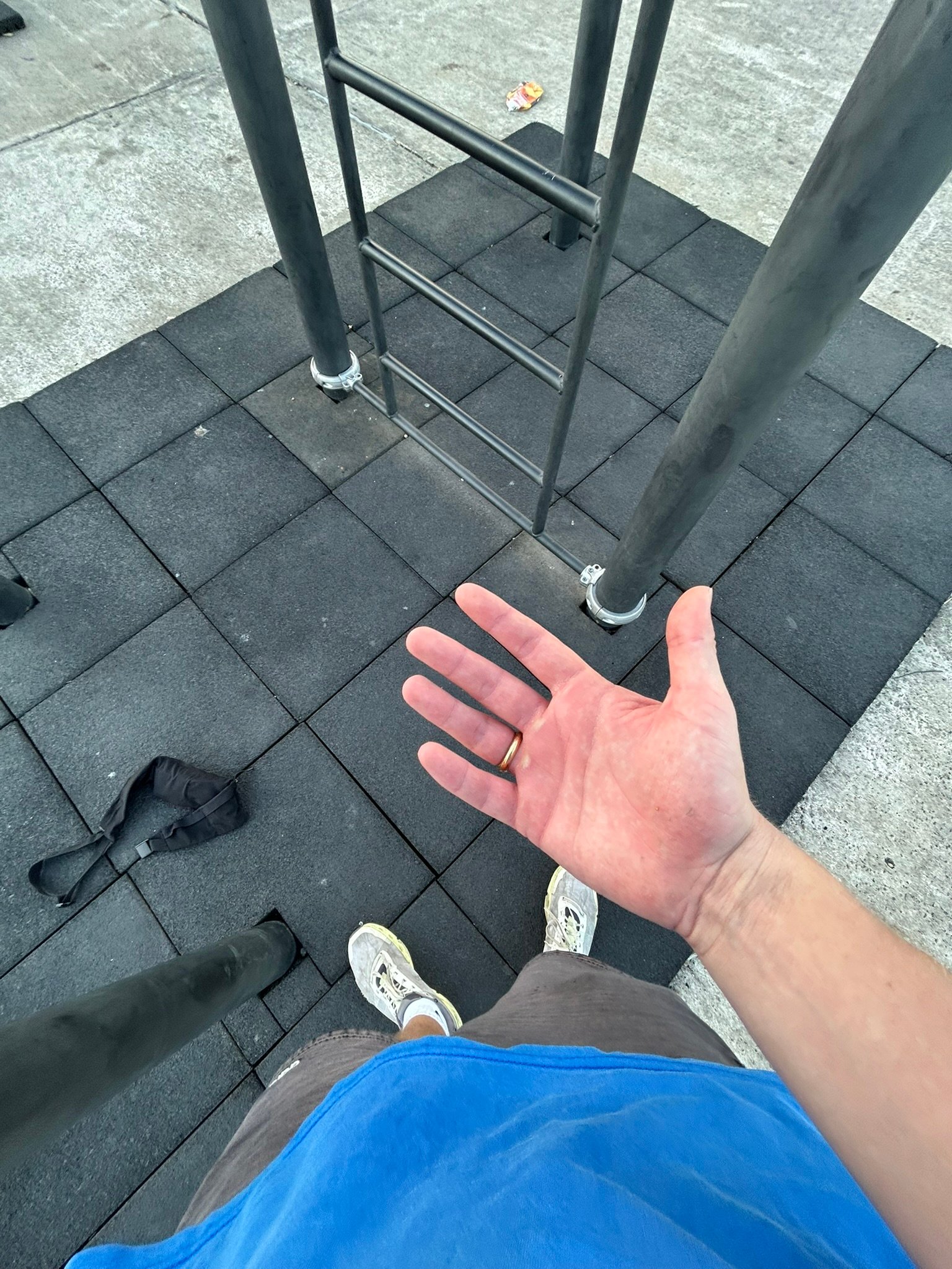 Man’s outstretched hand at an outdoor gym with rubber flooring, a harness, and climbing bars visible.
