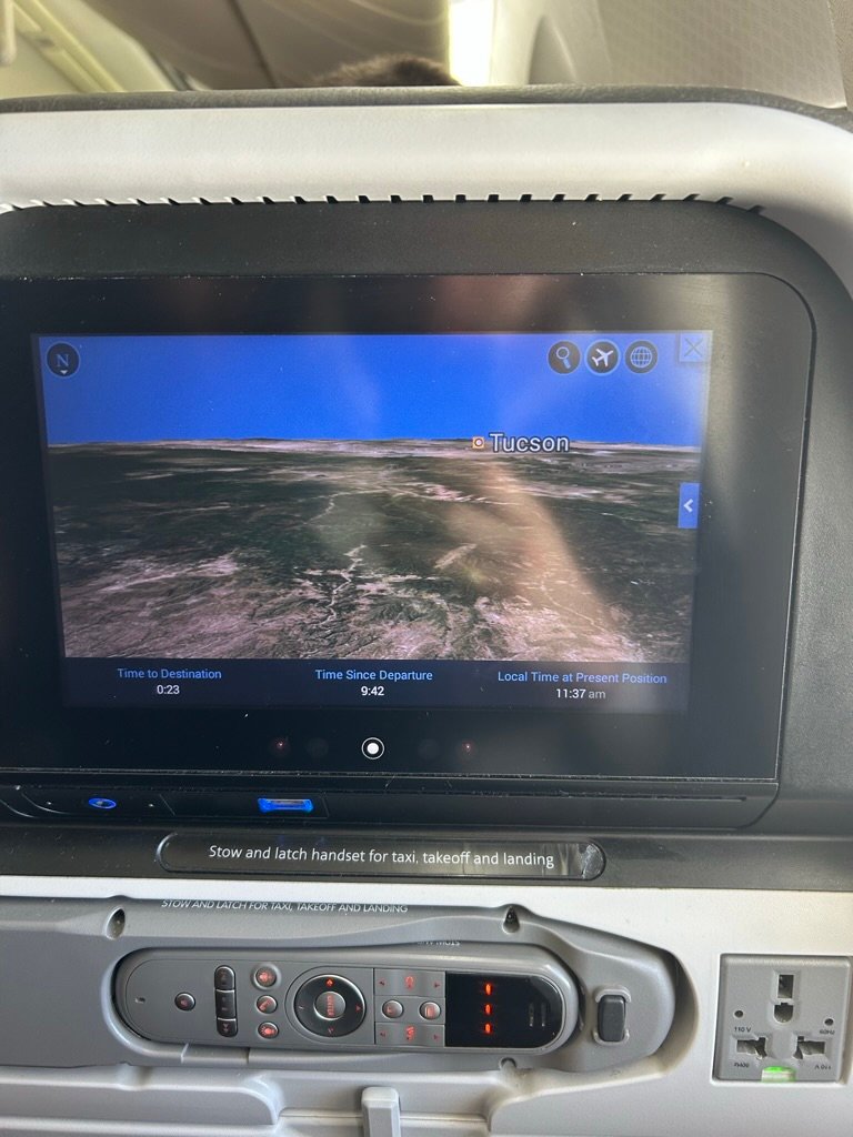 Airplane seatback screen showing a flight map approaching Tucson, Arizona, with flight details displayed.