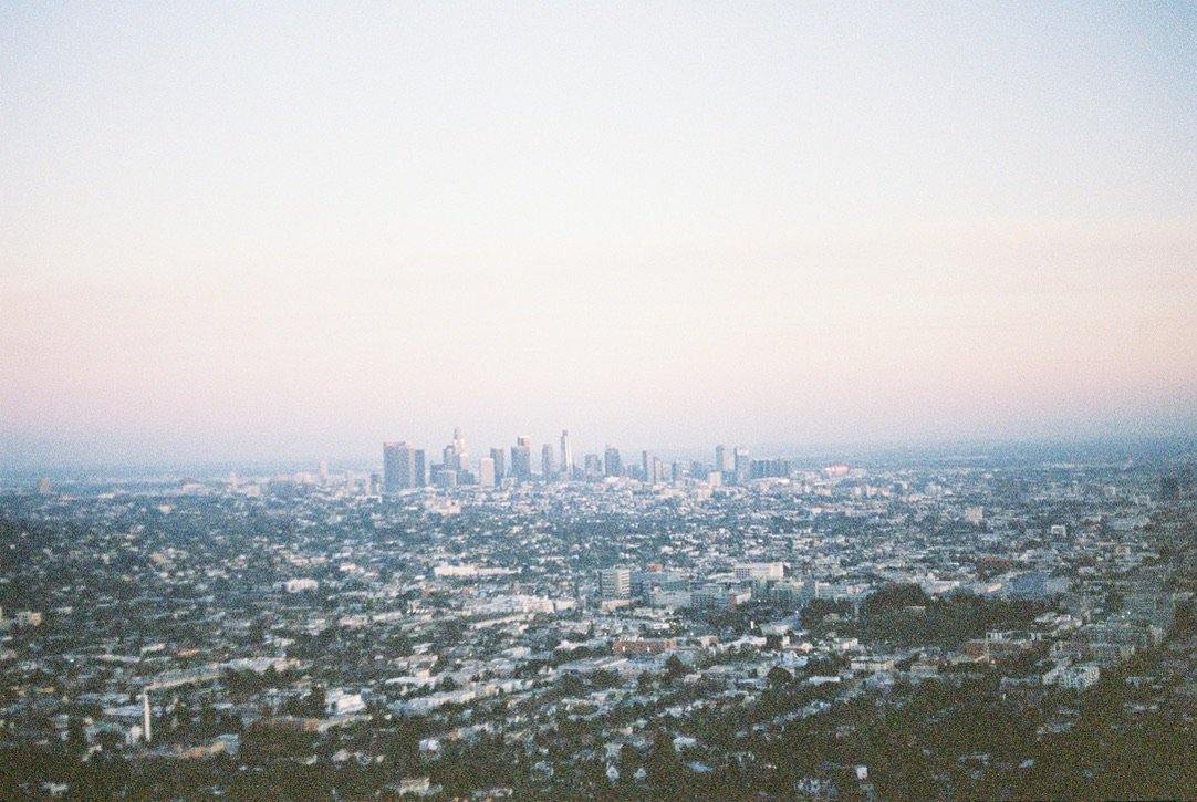 A wide, softly focused view of a sprawling city skyline at dusk, with a faint pink and blue sky overhead.