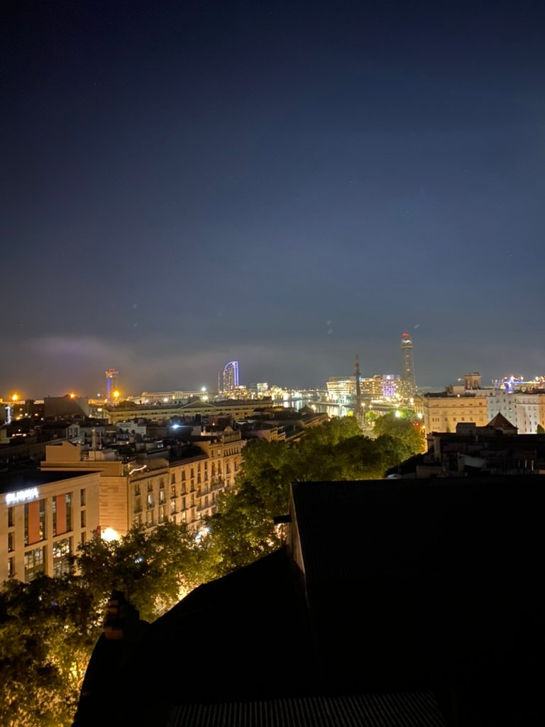 A city skyline at night with glowing lights from buildings, streets, and towers under a deep blue sky