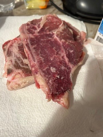 Two raw pieces of red meat placed on a white paper towel under bright kitchen lighting