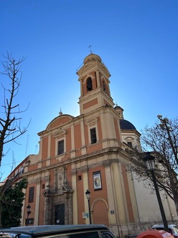 A warm-toned European church with a bell tower, glowing under a bright blue sky with bare trees nearby