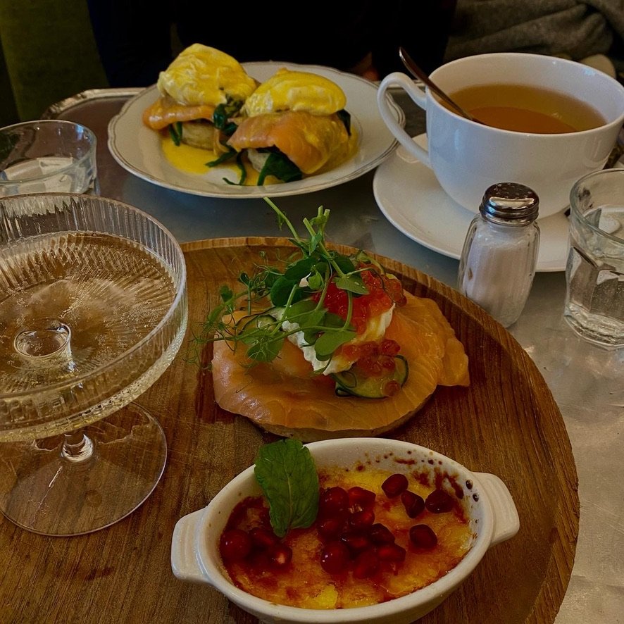 A brunch table with smoked salmon, eggs benedict, dessert with pomegranate, tea, and sparkling water.