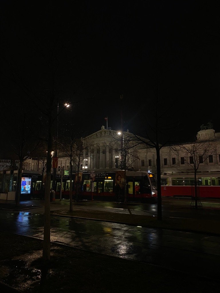 A city street at night with a tram passing by and a historic building illuminated in the background.