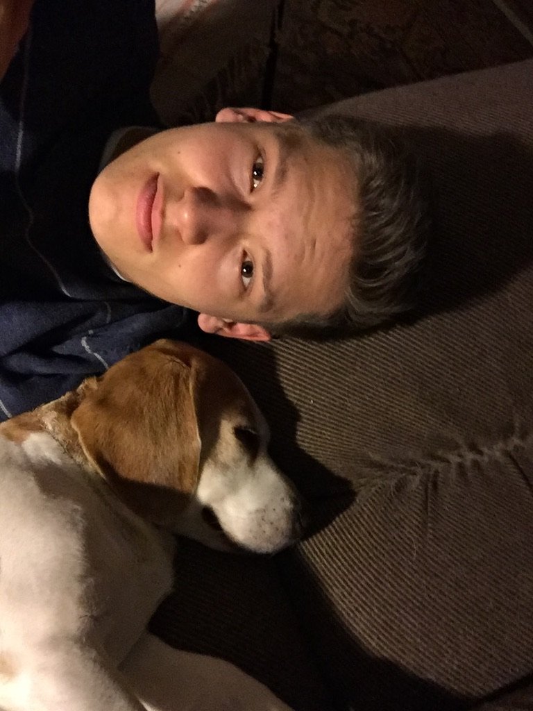 A young man lies on a couch beside a sleeping beagle, both appearing peaceful and relaxed.