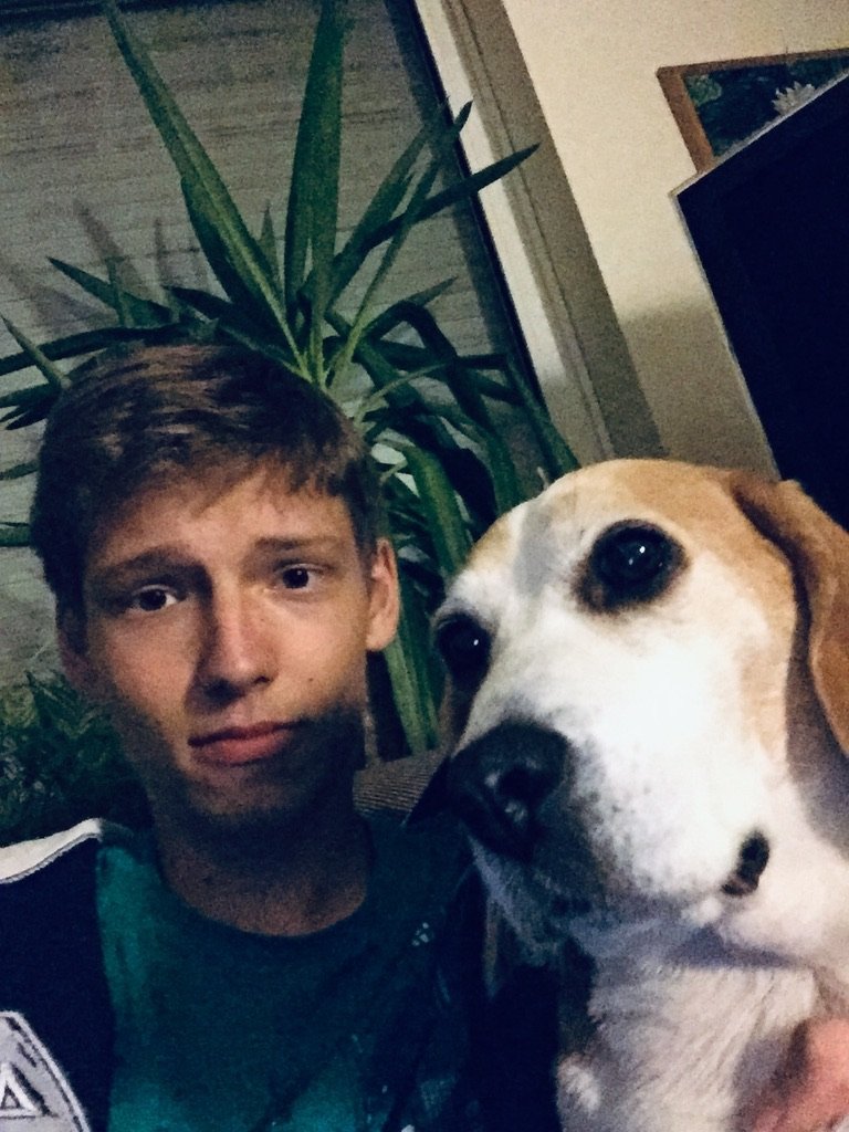 A young man sits indoors next to a beagle, both looking into the camera with a calm expression.