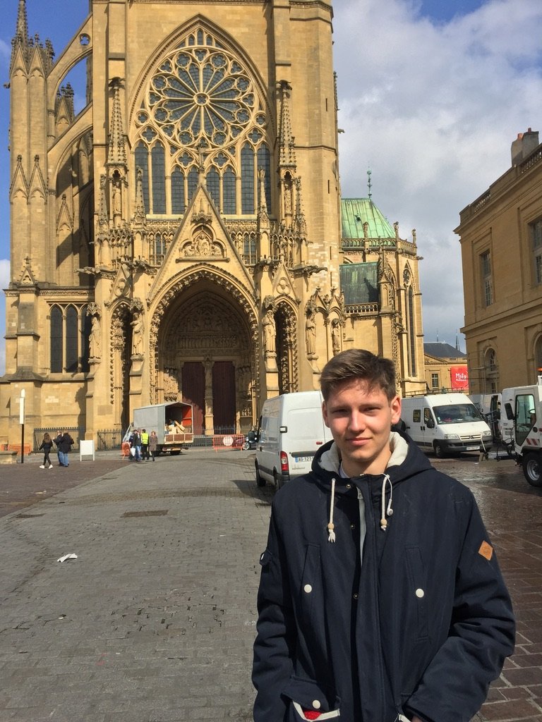 A young man stands in front of a grand Gothic cathedral with intricate architecture and a large rose window
