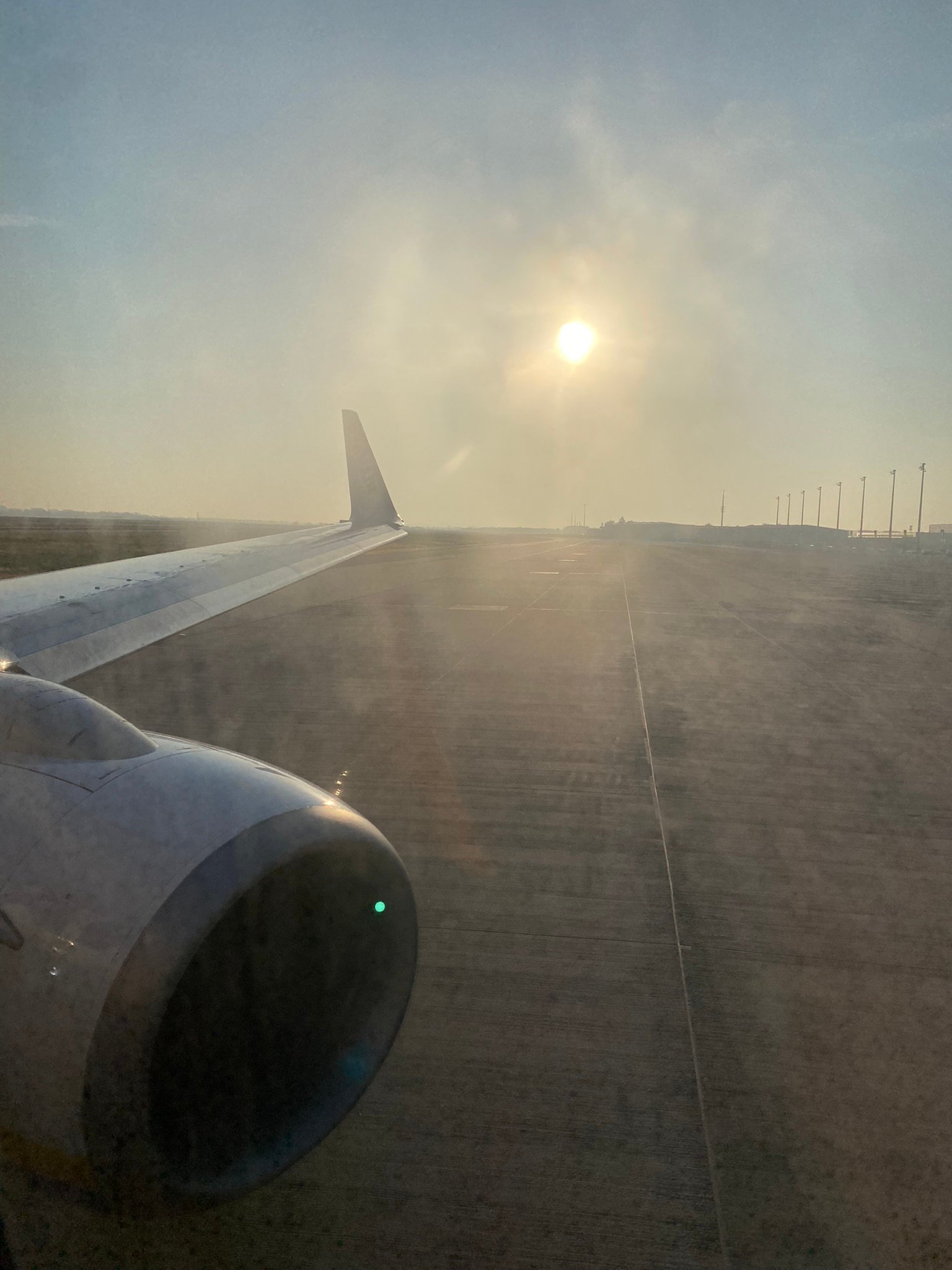 View from an airplane window showing the wing and engine during sunrise on a quiet runway
